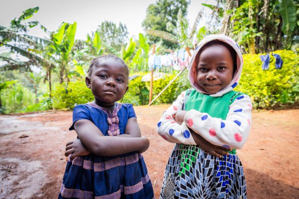 Two African female toddler friends standing outdoors in the village.